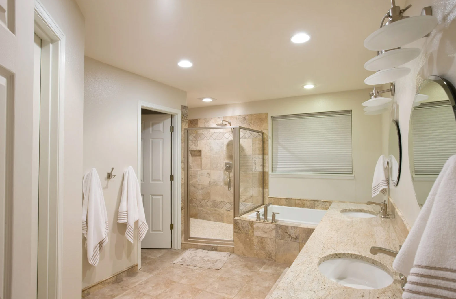 Modern bathroom with double sinks, a glass shower, a bathtub, and white towels hanging on the wall.
