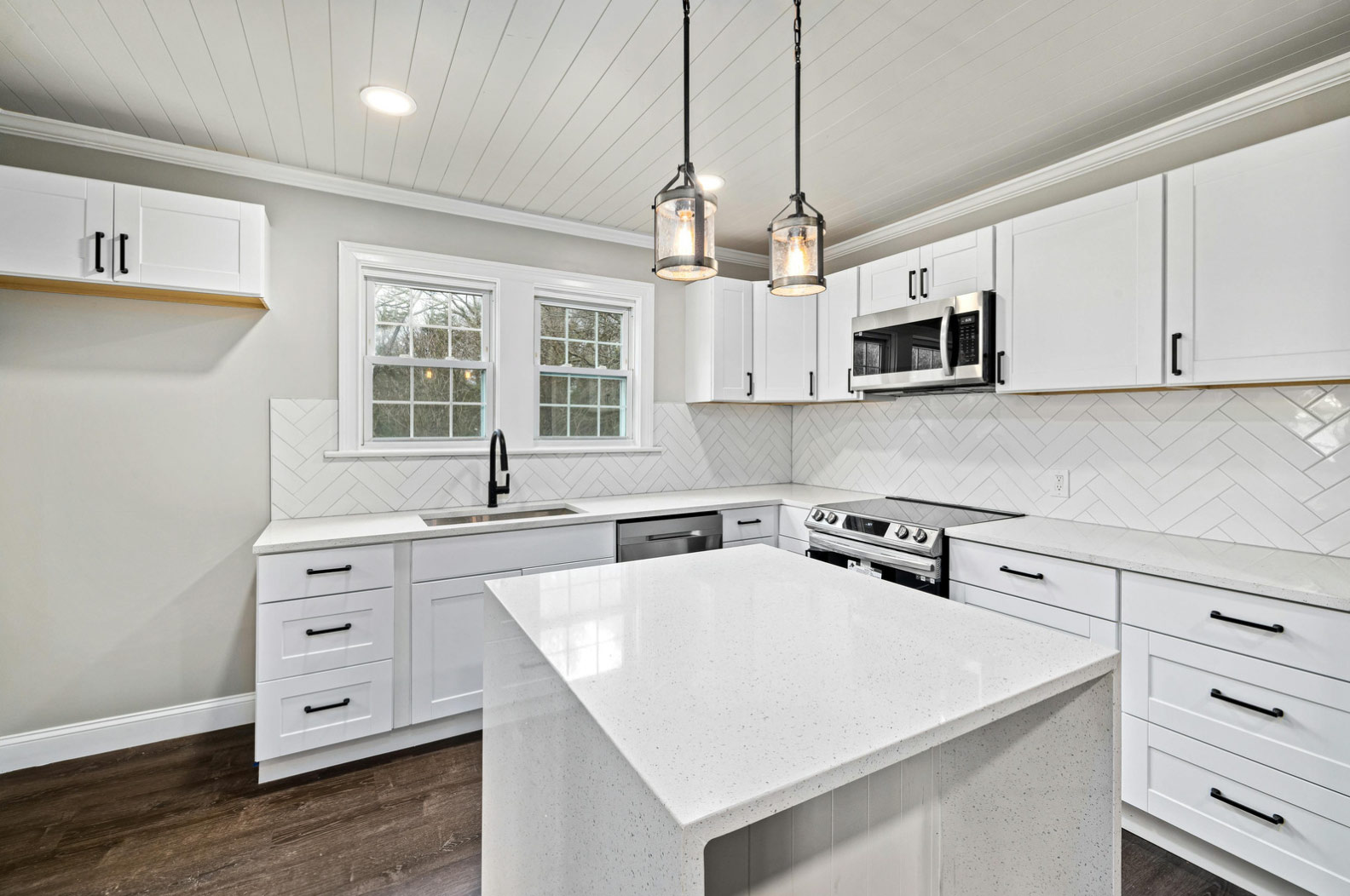 Modern white kitchen with an island, stainless steel appliances, and pendant lights over the counter.