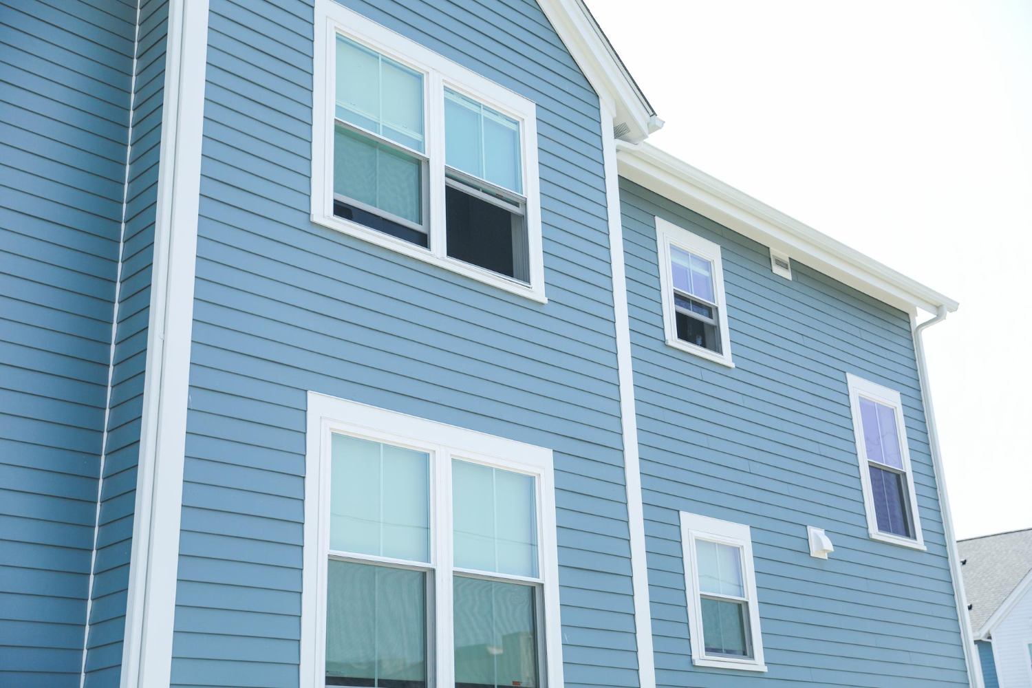 Blue house with white trim, showing several windows from a low angle on a bright, sunny day.